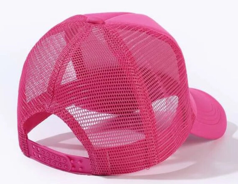 May include: A pink mesh trucker hat with a solid pink front panel and a mesh back panel. The hat has a curved brim and an adjustable strap.