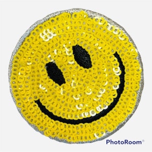May include: A yellow smiley face patch made of sequins. The patch has a black outline and a black smile.