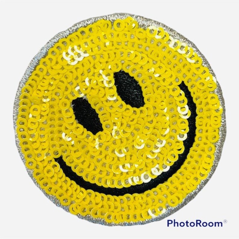 May include: A yellow smiley face patch made of sequins. The patch has a black outline and a black smile.