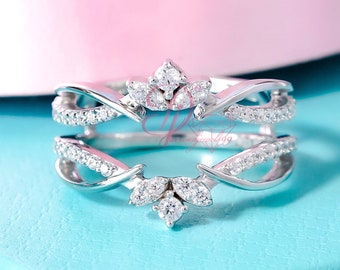 May include: A silver ring with a delicate, intertwined design featuring small, clear gemstones. The ring has a crown-like detail at the top, adding a touch of elegance.