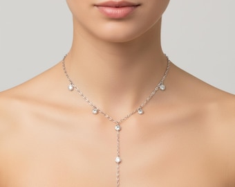 May include: A silver necklace with multiple clear, round gemstones. The necklace has a delicate chain design with gemstones dangling at various points, including a vertical drop of stones.