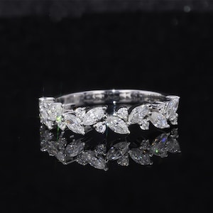 Op de afbeelding: Een zilveren ring met een bladeren ontwerp. De ring heeft marquise-geslepen en ronde heldere edelstenen in een herhalend patroon rond de band. De ring wordt gepresenteerd op een reflecterend zwart oppervlak.