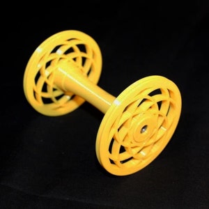 Può includere: Un'aspo di plastica gialla con un design geometrico decorativo su ciascuna estremità. L'aspo viene utilizzato per avvolgere filato o filo.