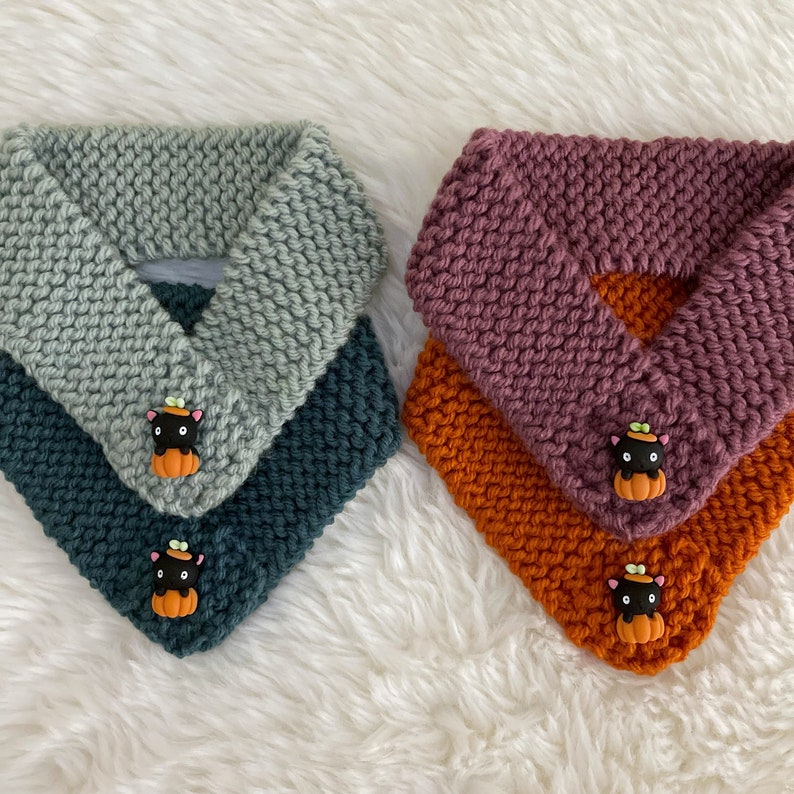 Peut inclure: Deux chauffe-cou  tricot&eacute;es avec un motif de chat noir et de citrouille. Un chauffe-cou est bleu sarcelle et vert, l'autre est orange et marron.