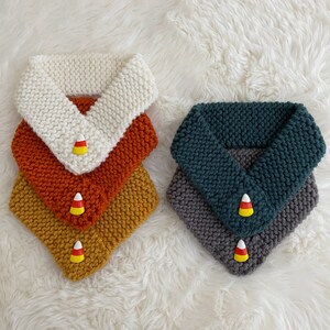 Peut inclure: Quatre tours de cou en tricot empilés, avec la couche supérieure blanche, la deuxième couche orange, la troisième couche jaune et la couche inférieure grise. Chaque couche a un motif de maïs sucré.