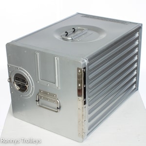 May include: A silver metal storage box with a hinged lid and a handle on the side. The box has a ribbed design on the side and a small round window on the front.