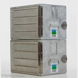 Könnte beinhalten: Zwei gestapelte Metall-Aufbewahrungsbehälter im Industriestil. Jeder Behälter hat eine rechteckige Form mit horizontalen Rillen auf der Vorderseite. Die Behälter sind silberfarben mit Griffen, Verschlüssen und einem "LEVEL"-Aufkleber.