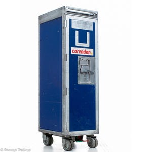 May include: A blue and silver airline service cart with the "corendon" logo. The cart has a metal frame, blue panels, a handle, and four wheels. The cart is designed for in-flight service.