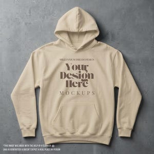May include: A beige hooded sweatshirt featuring long sleeves, a front kangaroo pocket, and dark brown text printed on the chest that reads: MILLENNIUM DREAM DESIGN, YOUR DESIGN HERE, MOCKUPS.