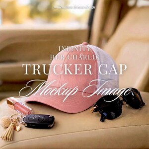 May include: A pink trucker cap with a white mesh back, featuring the text INFINITY HER CHARLIE TRUCKER CAP Mockup Image. Beside the cap are black sunglasses, a tube of lip gloss, and a black car key fob with a gold tassel keychain attached.