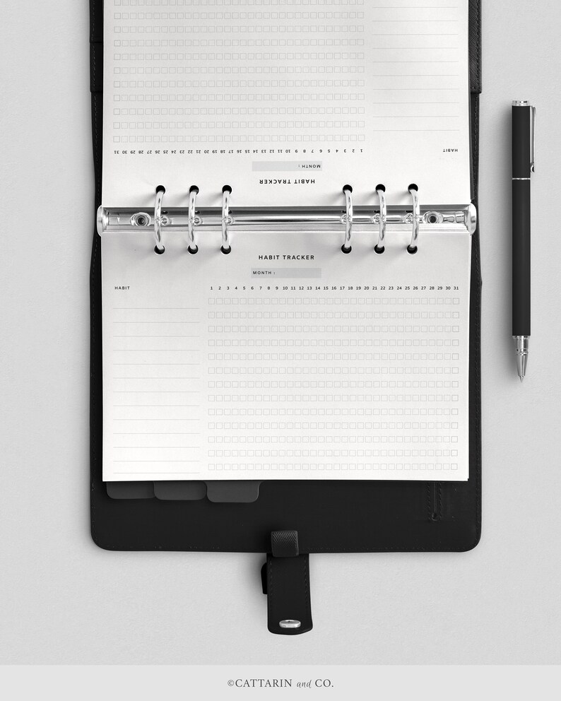 May include: A black binder with a white habit tracker page inside. The page has a grid of squares for tracking daily habits. The text "HABIT TRACKER" is printed at the top of the page.
