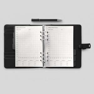 May include: A black leather bound planner with a silver ring binder. The planner is open to a page with a gridded section labeled "Credit Score Tracker" and a section for tracking credit score by month and quarter.