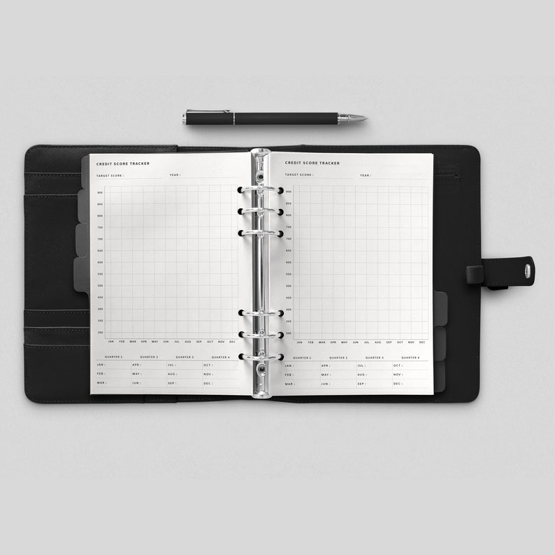May include: A black leather bound planner with a silver ring binder. The planner is open to a page with a gridded section labeled "Credit Score Tracker" and a section for tracking credit score by month and quarter.