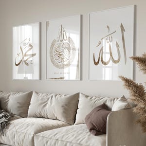 Puede incluir: Tres impresiones artísticas enmarcadas con caligrafía árabe dorada cuelgan sobre un sofá beige. Las impresiones presentan una escritura elegante en varios diseños, incluyendo la palabra "Muhammad" y el nombre "Allah". La obra de arte añade un toque de sofisticación al salón.