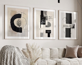 May include: Three framed black and white abstract art prints featuring Arabic calligraphy. The prints are hung on a white wall above a white sofa with a throw blanket and a coffee table.
