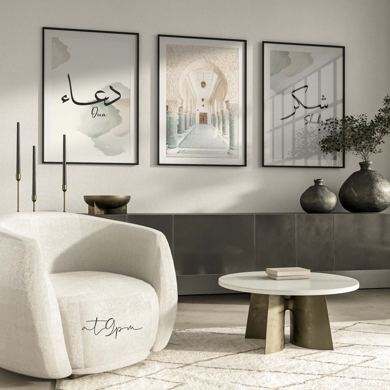 May include: Three framed prints on a white wall. The center print shows a hallway with arched doorways and columns. The left print features the Arabic word "Dua" in black calligraphy with a watercolor background. The right print features the Arabic word "Shukr" in black calligraphy with a watercolor background.