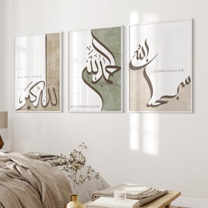 May include: Three framed art prints featuring Arabic calligraphy in brown and beige hues. The prints display phrases such as "Allah-u Akbar," "Alhamdulillah," and "Subhanallah." The artwork is hung above a bed with a neutral-toned duvet.