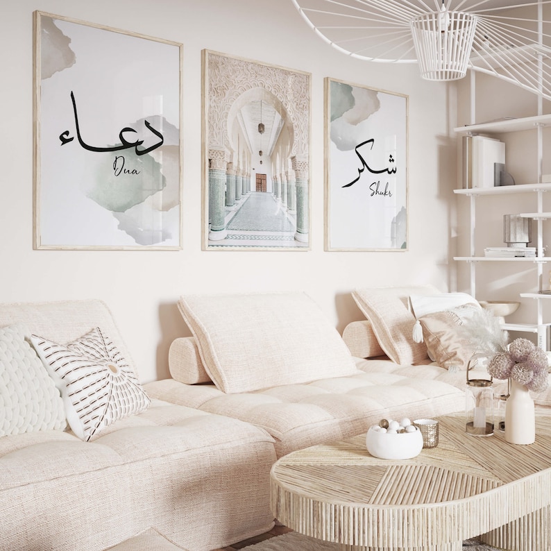 May include: Three framed prints with Arabic calligraphy and a photograph of an arched hallway. The prints are hung on a white wall above a light beige couch with white pillows.