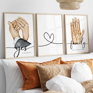 May include: Three framed prints with watercolor illustrations of hands. The first print shows two hands holding each other with a ring on one finger. The text "yes" and "15. November 2018" is below the hands. The second print shows a simple heart shape drawn with a black line. The third print shows four hands holding each other. The text "family" is below the hands with the names "David, Kathi, Emilia, Jolien" underneath.