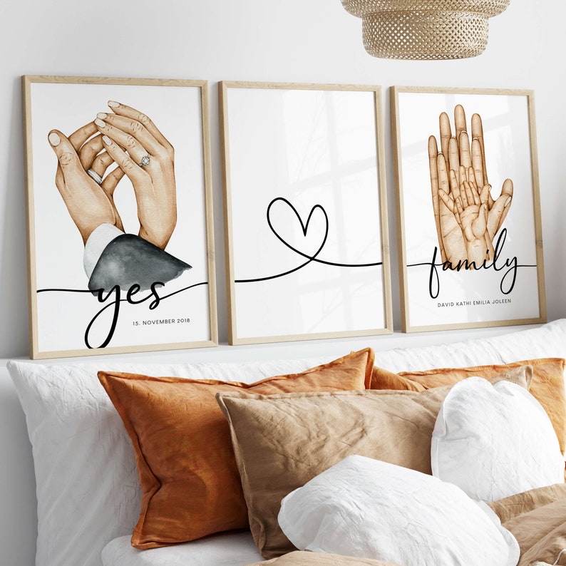 May include: Three framed prints with watercolor illustrations of hands. The first print shows two hands holding each other with a ring on one finger. The text "yes" and "15. November 2018" is below the hands. The second print shows a simple heart shape drawn with a black line. The third print shows four hands holding each other. The text "family" is below the hands with the names "David, Kathi, Emilia, Jolien" underneath.