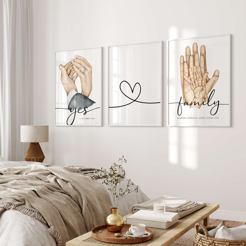 May include: Three white framed prints with black calligraphy. The left print shows a watercolor illustration of two hands holding a ring with the word "yes" and the date "12 NOVEMBER 2018". The middle print shows a simple heart shape with a line underneath. The right print shows a watercolor illustration of four hands with the word "family" and the names "MARCEL DORATA LEON LUKAS LEA".