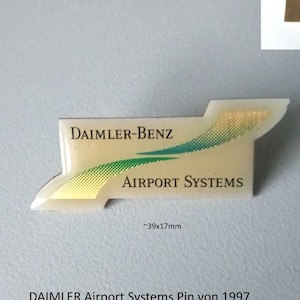 Può includere: Uno spillo dorato e bianco con il testo "DAIMLER-BENZ" e "AIRPORT SYSTEMS". Lo spillo misura circa 39 mm x 17 mm.