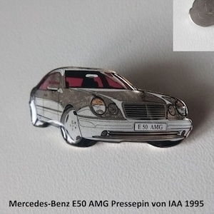 Peut inclure: Une épingle en métal argenté représentant une Mercedes-Benz E50 AMG blanche. L'épingle mesure environ 37 mm sur 18 mm et porte le texte "E 50 AMG" sur la plaque d'immatriculation de la voiture. L'épingle est une épingle à pression de l'IAA 1995.