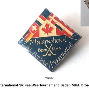 Peut inclure: Une épingle en émail bleu et blanc avec le texte "7th International '82 Pee-Wee Tournament Baden MHA" et un graphique de bâton de hockey et de rondelle. L'épingle est en forme de diamant et présente des drapeaux de différents pays.