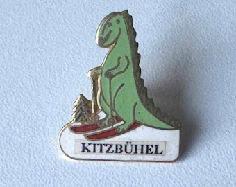 Wear Kitzbuehel – Rare Enamel Pin with Skiing Dinosaur Comic Design