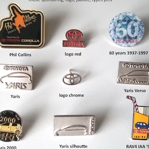 Può includere: Una collezione di spille per auto Toyota vintage, tra cui una spilla di Phil Collins, una spilla Yaris, una spilla Yaris Verso, una spilla Yaris 2000, una spilla Yaris silhouette, una spilla RAV4 IAA '95, una spilla logo rossa e una spilla logo cromata. Le spille sono disposte su uno sfondo bianco.
