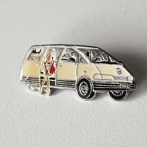 Könnte beinhalten: Ein silberfarbener Emaille-Pin in Form eines cremefarbenen Minivans mit schwarzen Rädern. Eine Figur in roter Jacke und weißem Kleid steht in der offenen Tür. Der Pin hat ein detailliertes Design und ist vor einem weißen Hintergrund platziert.