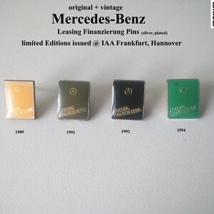 May include: Four silver plated Mercedes-Benz Leasing Finanzierung pins. The pins are in the shape of a book with the Mercedes logo on the front. The pins are from 1989, 1991, 1992, and 1994.  The pins are displayed on a white background.