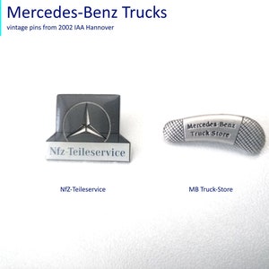 Könnte beinhalten: Zwei silberne Mercedes-Benz LKW-Pins. Der erste Pin zeigt das Mercedes-Benz Logo und den Text "Nfz-Teileservice". Der zweite Pin ist truckförmig und trägt den Text "Mercedes-Benz Truck Store".