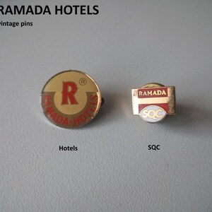 May include: Two vintage gold-coloured pins with the Ramada Hotels logo. The first pin is round and features a red "R" inside a gold circle with the words "Ramada Hotels" in red around the circle. The second pin is rectangular and features the words "Ramada" in red on a white background with the letters "SOC" in white on a red background.