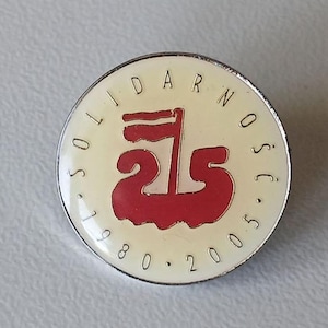 May include: A white and silver pin with the text "Solidarność" and the number "25" in red. The pin commemorates the 25th anniversary of the Solidarity movement in Poland, 1980-2005.