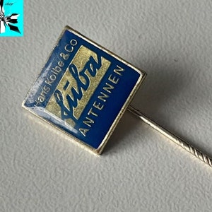 Puede incluir: Un pin de solapa de esmalte azul y dorado con el texto "Hans Kolbe & Co füba ANTENNEN" sobre un fondo blanco. El pin mide aproximadamente 13 mm.