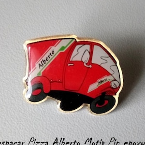 May include: A red and white Vespa-style delivery truck with the word "Alberto" on the side. The truck is a pin with a gold-coloured backing. The pin is a vintage item from the 1990s.