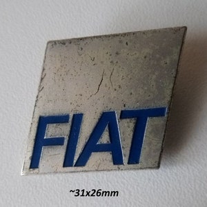 Op de afbeelding: Een zilverkleurige, gegraveerde FIAT-logo broche met blauwe letters. De broche is ongeveer 31 mm bij 26 mm.