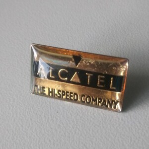 Könnte beinhalten: Eine goldene und schwarze Werbean Nadel für Alcatel, ein Telekommunikationsunternehmen. Die Nadel trägt die Aufschrift "Alcatel The Highspeed Company".