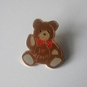 Puede incluir: Un oso de peluche marr&oacute;n con una pajarita roja y un pin dorado que dice "Amo Berl&iacute;n".