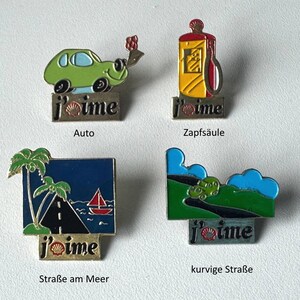 Può includere: Quattro spille smaltate con la scritta "j'aime". I disegni includono un'auto verde, un distributore di benzina giallo, una strada sul mare con una barca a vela e una strada tortuosa con un'auto. Ogni spilla ha un testo tedesco diverso.