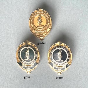 May include: Three gold-coloured and black enamel Olympic pins. The pins feature the text "1996 Centennial Olympic Games Atlanta Georgia Olympic Security Team". The pins are oval-shaped with a torch and Olympic rings design.