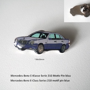 May include: A blue and silver enamel pin of a Mercedes-Benz E-Class Series 210 car. The pin is approximately 1.5 inches wide and 0.6 inches tall. The text "Mercedes-Benz E-Klasse Serie 210 Motiv Pin blau" and "Mercedes-Benz E-Class Series 210 motif pin blue" is printed below the pin.
