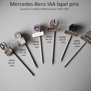 Può includere: Sei spille da bavero Mercedes-Benz argentate e blu con il testo "IAA" e l'anno del Salone di Francoforte, dal 1983 al 1987.