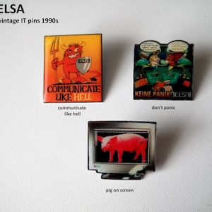 Peut inclure: Trois épingles vintage ELSA IT des années 1990. La première épingle représente un diable rouge avec une fourche et le texte "Communicate Like Hell". La deuxième épingle représente deux personnages de dessin animé avec des bulles de dialogue et le texte "Keine Panik! ELSA". La troisième épingle représente un cochon rose sur un écran d'ordinateur.