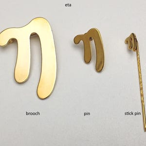 以下が含まれることがあります： 「m」の形をした、金色の金属製のピンが3つ、それぞれ異なるスタイルで並んでいます。最初のものは大きなブローチ、2番目は小さなピン、3番目はスティックピンです。