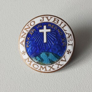 Peut inclure: Une épingle ronde dorée avec une bordure blanche et un design complexe. Le centre présente un fond bleu avec une croix blanche et du texte. L'épingle comprend le texte "ANNO JVBILAEI MCMXXV" et "PAX XPI IN REGNO XPI".