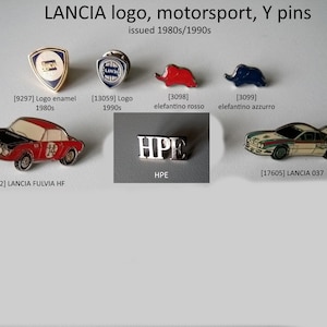Könnte beinhalten: Eine Sammlung von Vintage-Anstecknadeln mit LANCIA-Autologos, darunter ein roter und schwarzer LANCIA Fulvia HF, ein weißer LANCIA 037 und eine silberne LANCIA-Logo-Anstecknadel. Die Anstecknadeln stammen aus den 1980er und 1990er Jahren.