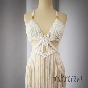 May include: White crochet top with a geometric design and long fringe. The top has gold accents and is displayed on a mannequin.