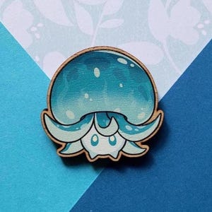 May include: Wooden pin featuring a cartoon jellyfish design. The jellyfish has a blue and white color scheme with a light brown wooden border. The pin is round and has a cute, friendly appearance.